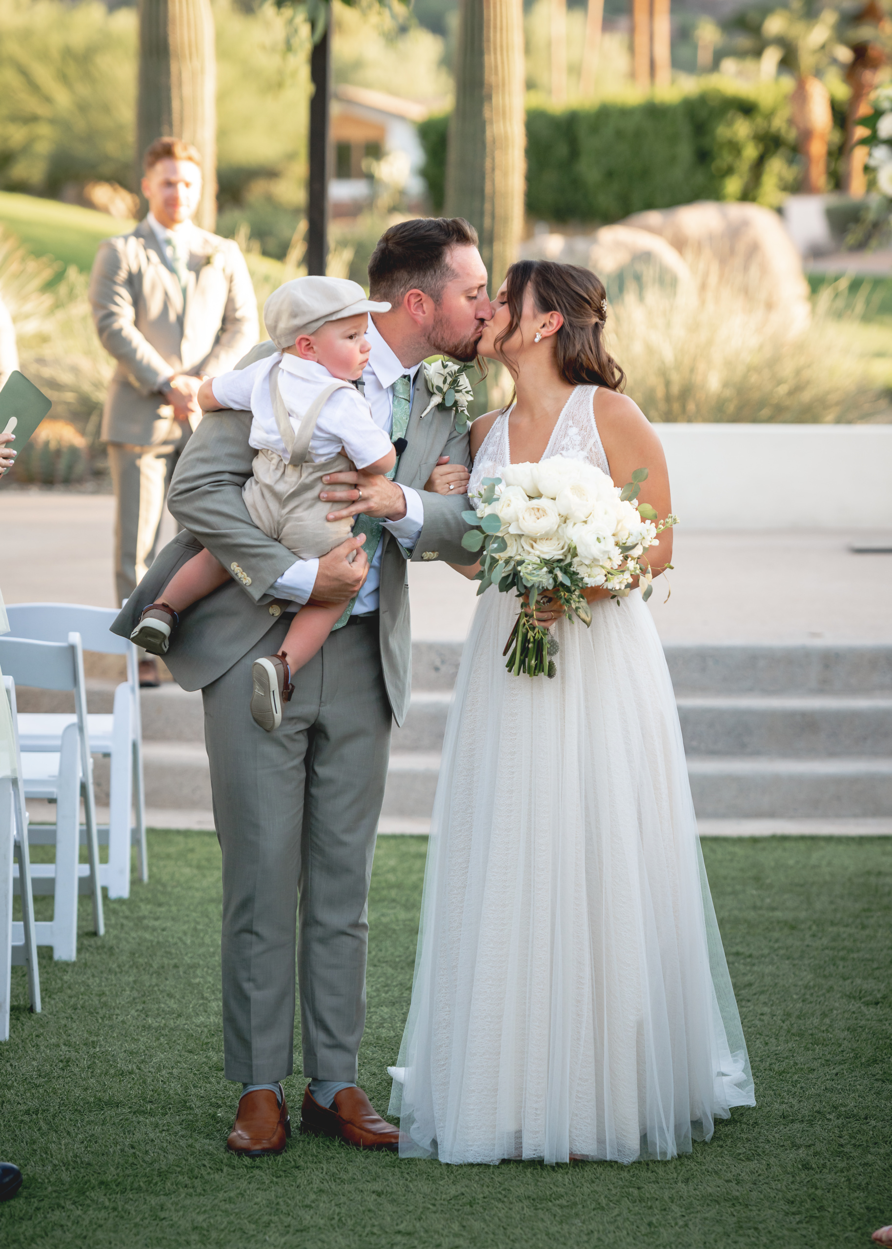 Newlyweds sharing a kiss with their child at an outdoor Scottsdale wedding ceremony