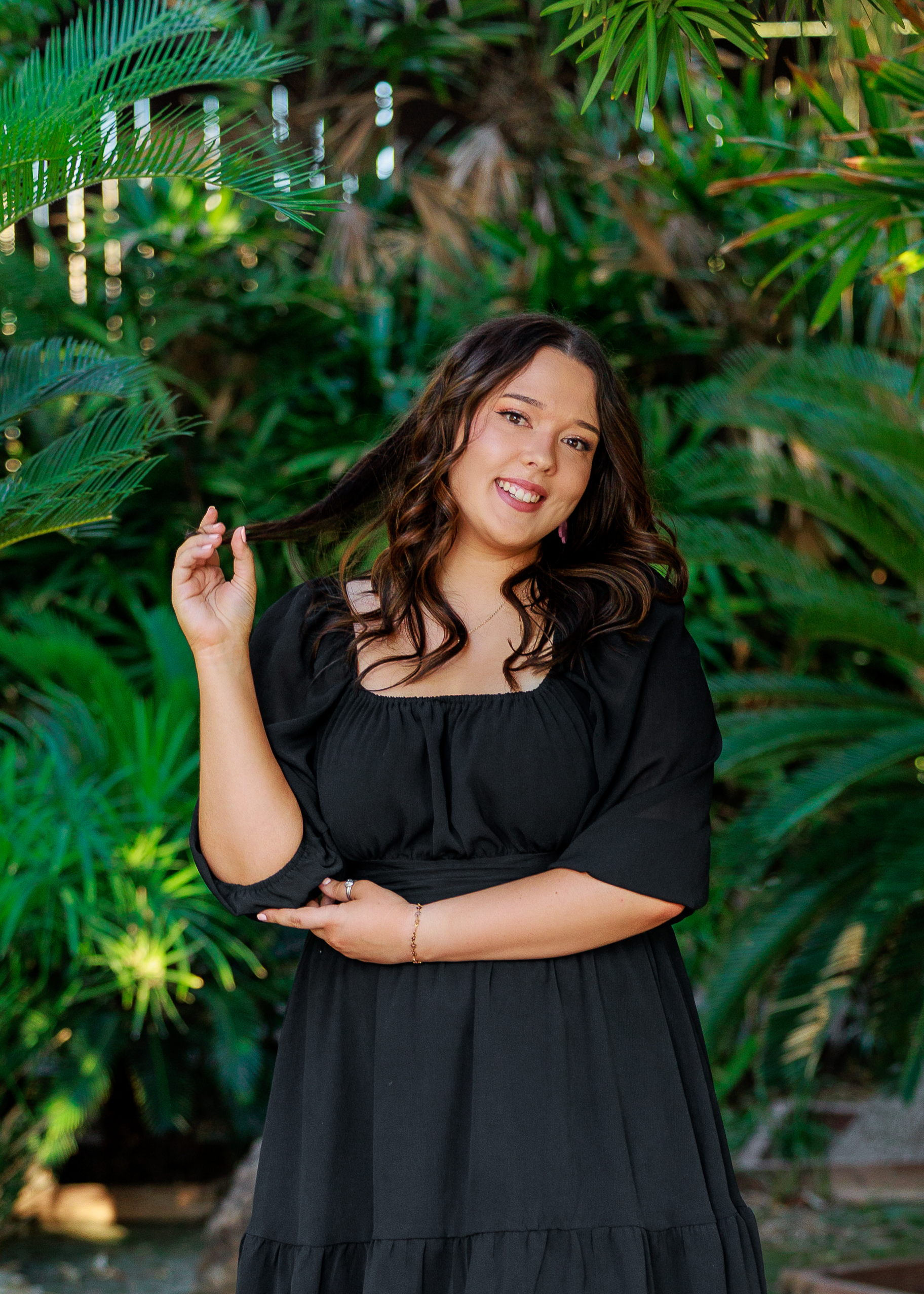 Maddie, our head photographer, smiling in an outdoor setting surrounded by lush greenery, showcasing her warm and approachable personality.